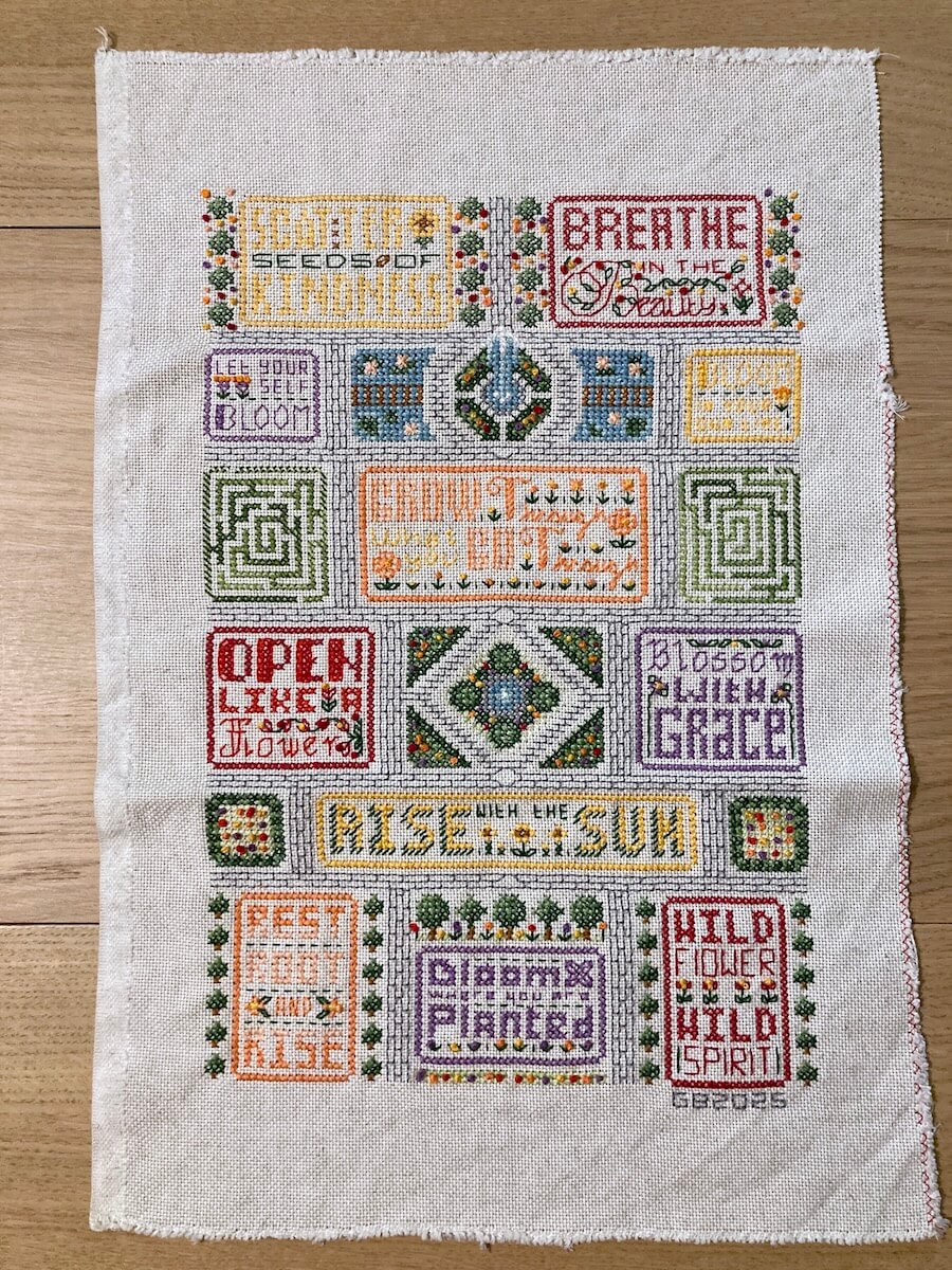 Moderner Stick-Sampler mit Sinnsprüchen, der wie eine englische Gartenanlage angelegt ist.